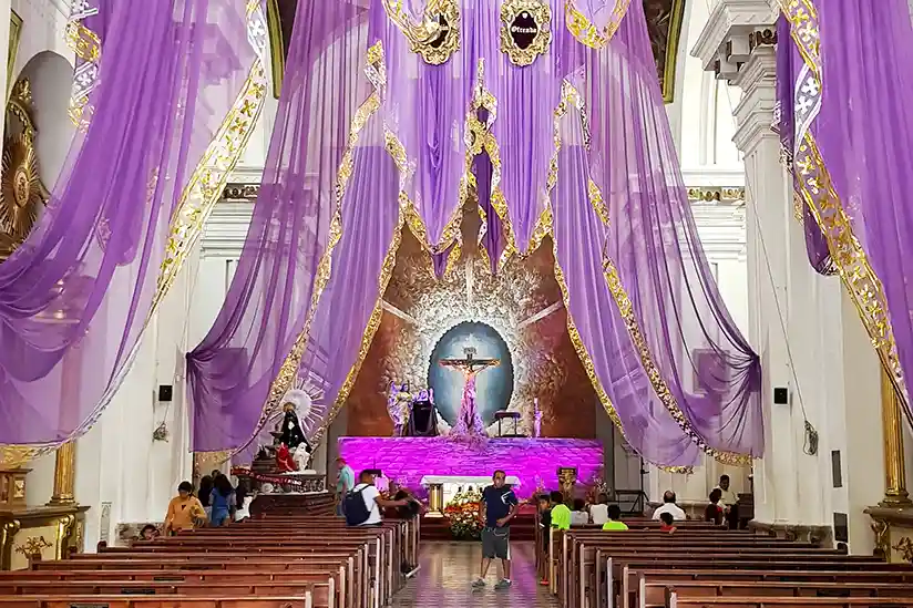 Festively decorated altar in a church with purple curtains and gold accents in celebration of Easter in Mexico.